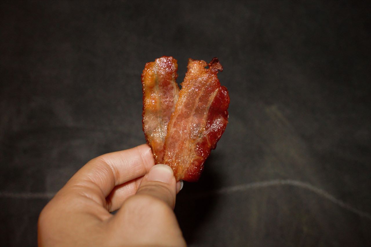 a hand holding perfectly crispy, oven baked bacon.
