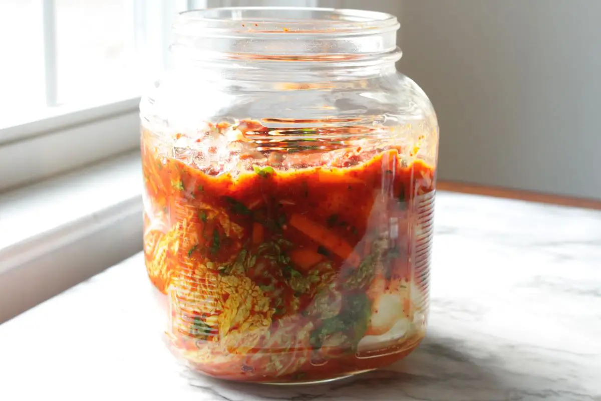 Kimchi in a glass jar on a marble surface.
